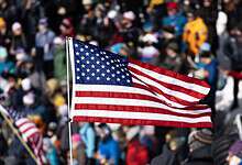 American flag waving at a crowded winter sports event with spectators in winter clothing.