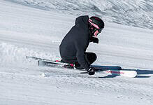 Skier in black winter gear carving through fresh snow on a clear day in the mountains.